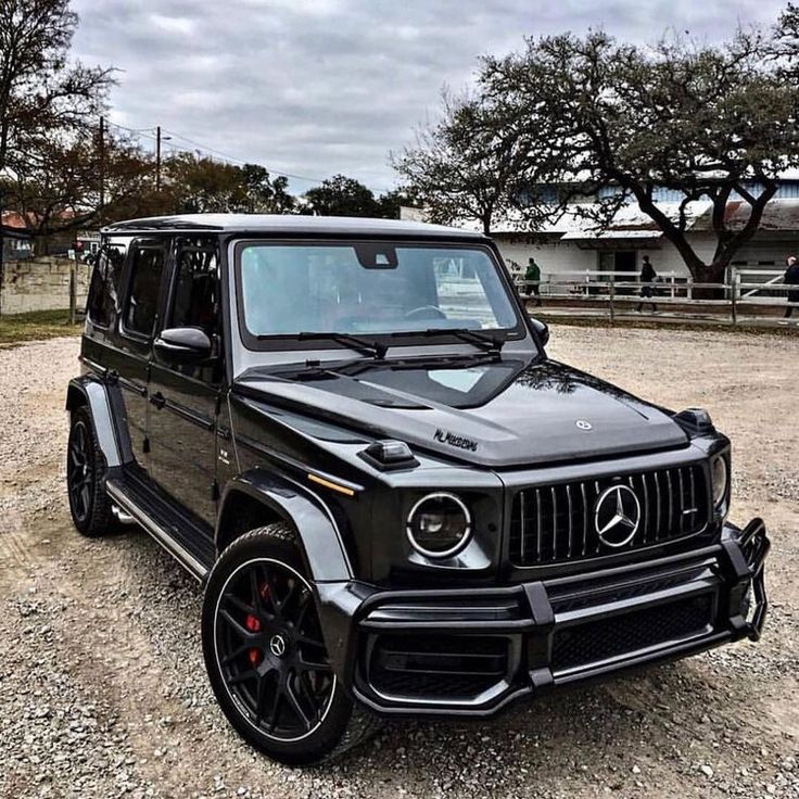 a black mercedes g - class is parked on gravel