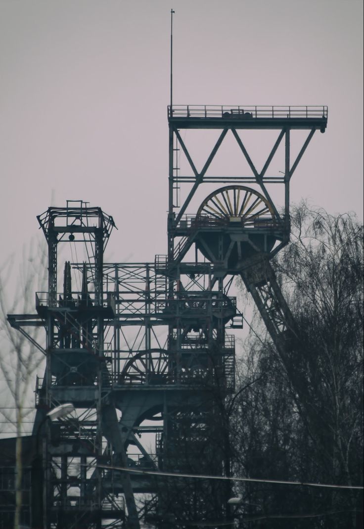 a large metal structure with a water wheel on it's side and trees in the background