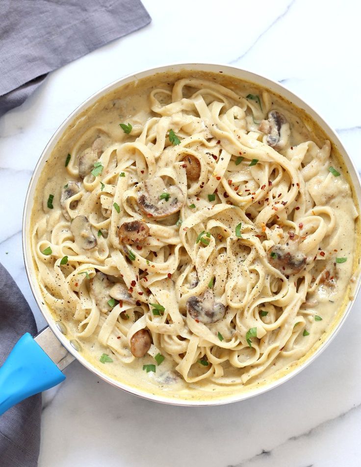 a pan filled with pasta and mushrooms on top of a white marble countertop next to a blue spatula