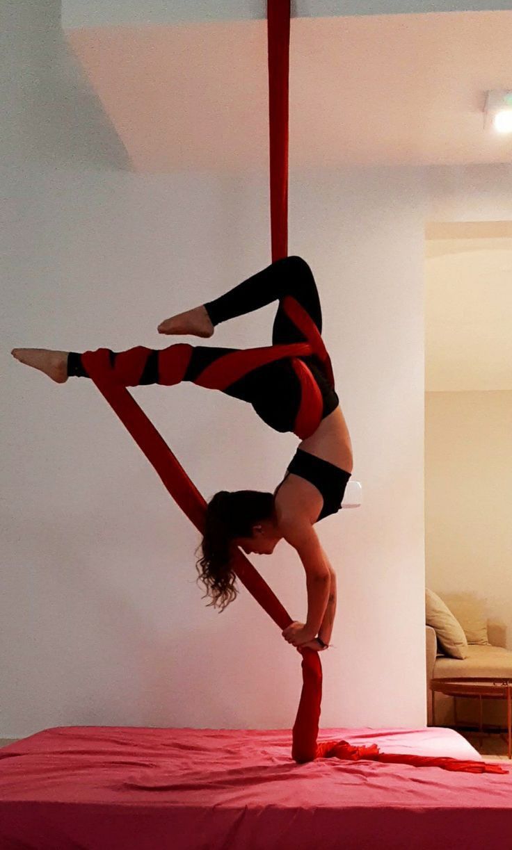 a woman is doing aerial acrobatic tricks on a red bed sheet in a room