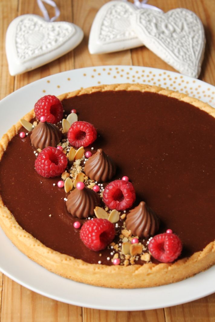 a chocolate tart with raspberries and nuts on top sits on a white plate