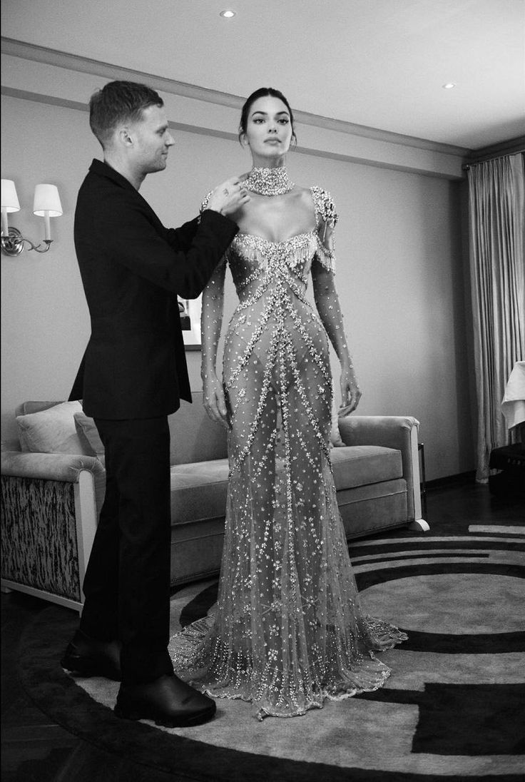 a man fixing the back of a woman's long sleeved dress in a living room