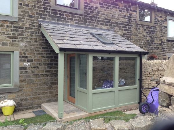 a small green shed sitting in front of a brick building next to a lawn chair