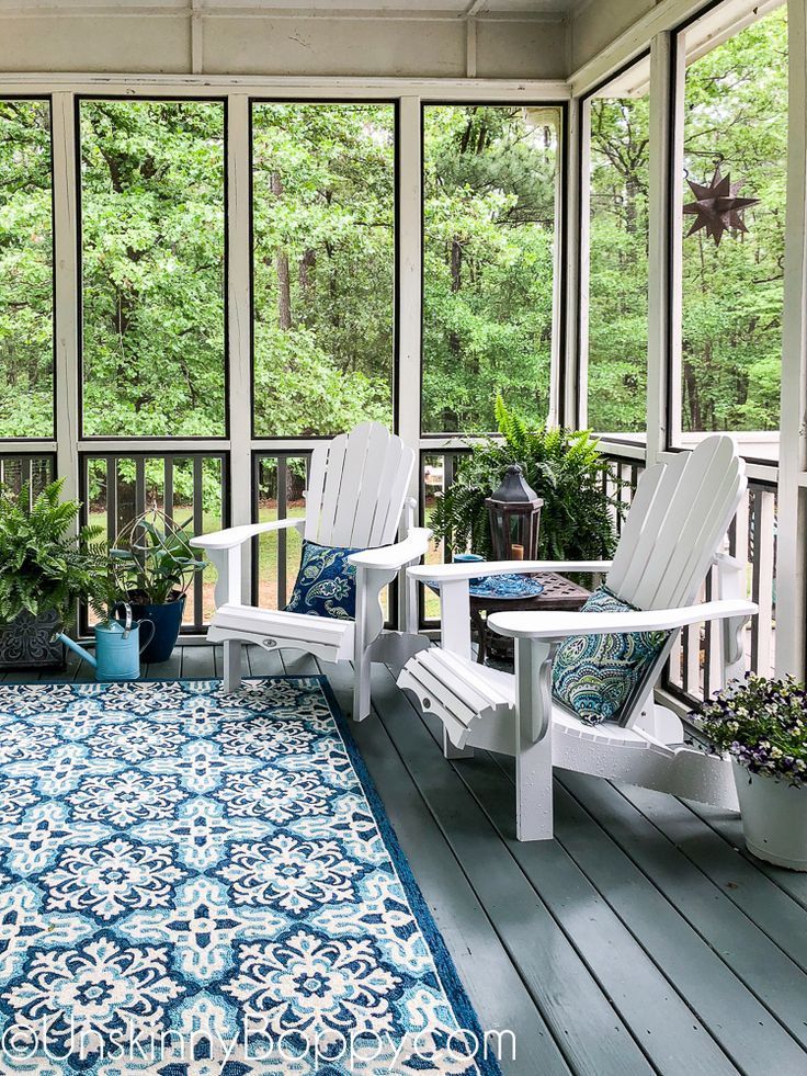 two white chairs sitting on top of a blue and white rug in front of windows