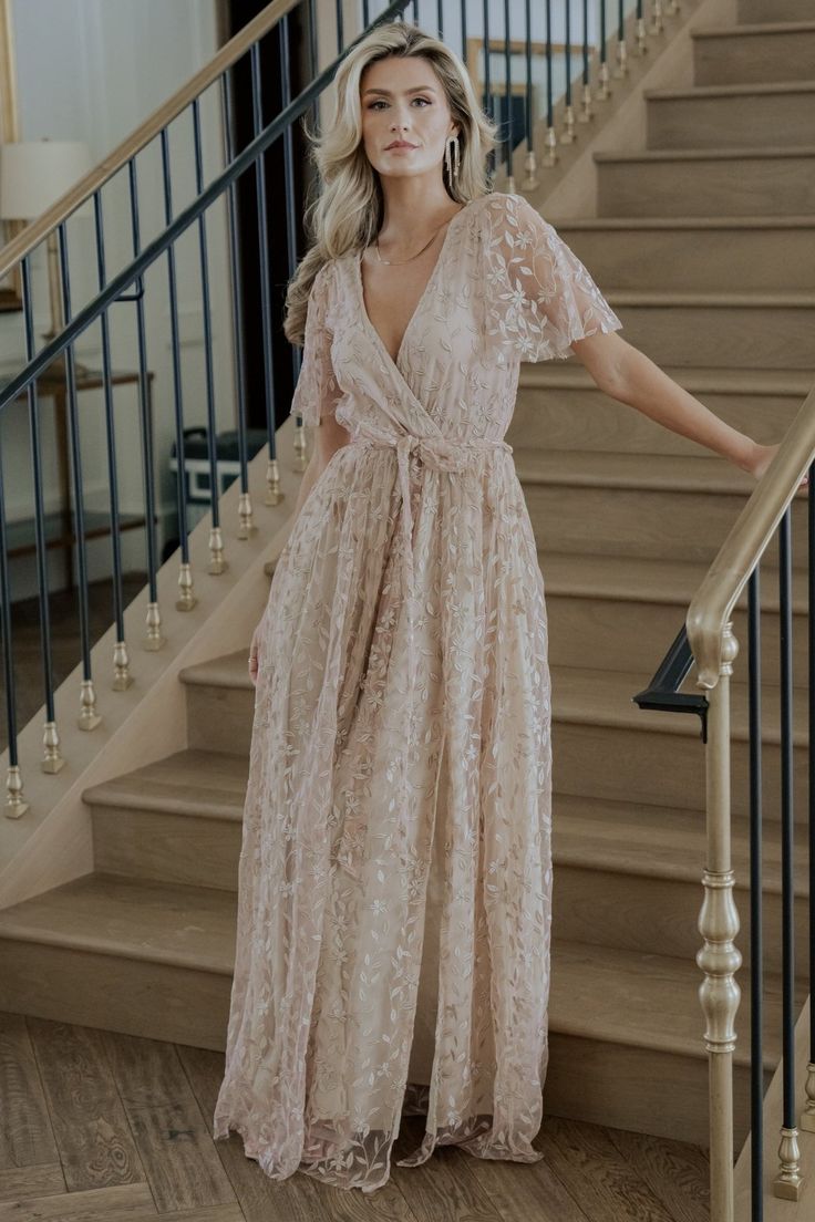 a woman standing in front of some stairs wearing a long dress with an open back