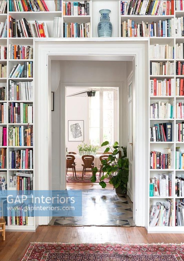 a room filled with lots of books on top of a white book shelf next to a doorway