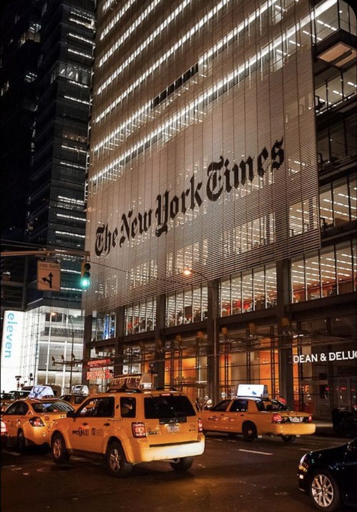 the new york times building is lit up at night with taxi cabs parked in front