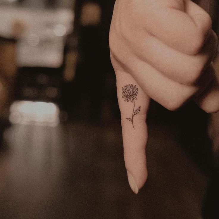 a person's finger with a small flower tattoo on it