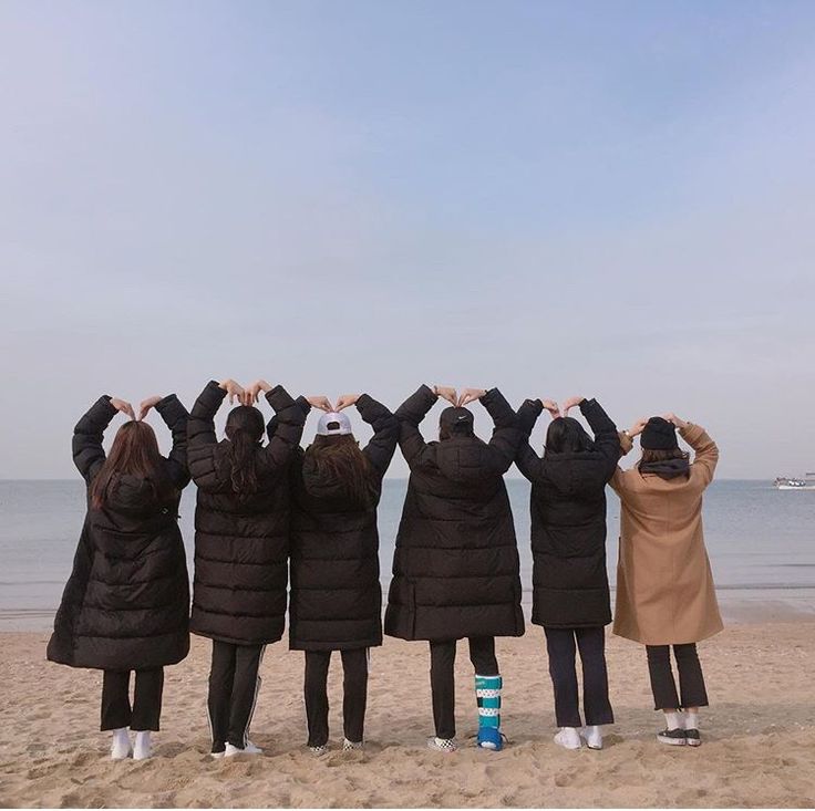 four people standing on the beach with their hands in the air and looking at the water