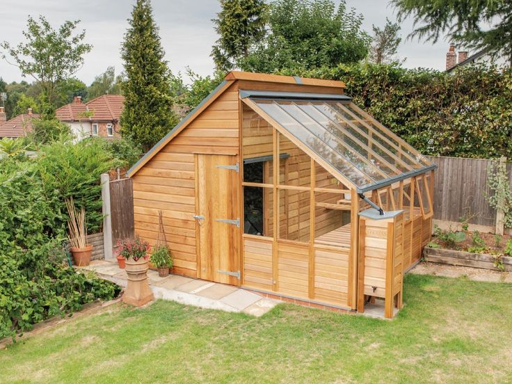 a small wooden shed with a glass roof and windows on the side, in a garden