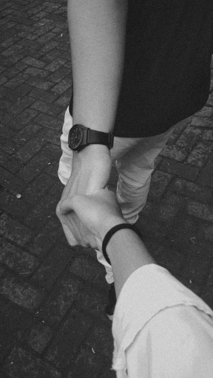 two people holding hands while walking down a brick road in black and whit photo