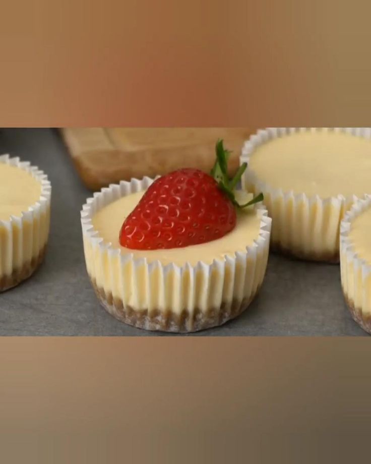 four cupcakes with white frosting and a strawberry on top are lined up