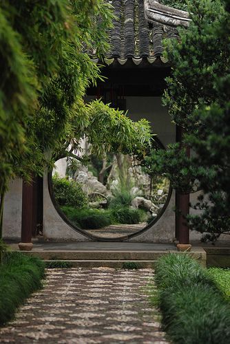 a circular mirror in the middle of a garden with trees and bushes around it,