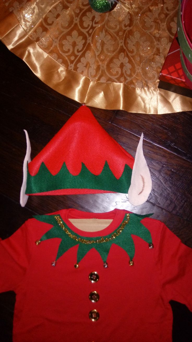 a child's red and green christmas outfit on a wooden floor next to other items