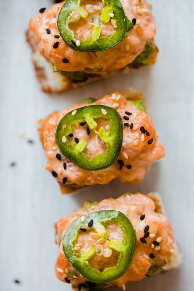 three sushi rolls with cucumbers and black sesame seeds on top, sitting on a white surface