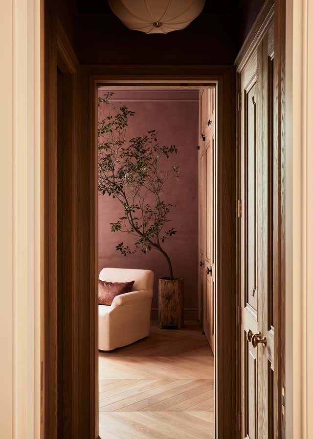 an open door leading to a living room with a tree in the corner and pink walls