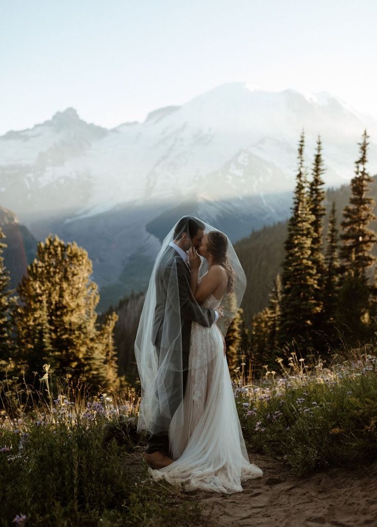 a bride and groom standing in the mountains with their wedding veil blowing in the wind