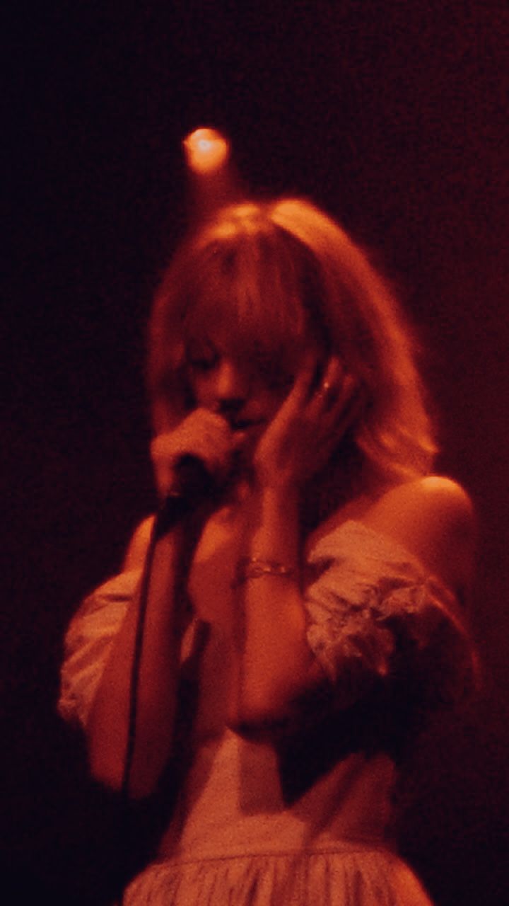 a woman standing in front of a microphone with her hands to her face while talking on the phone