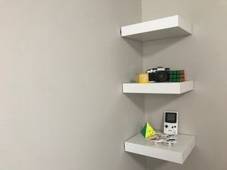 two white shelves with electronic devices on them in a corner next to a wall mounted camera