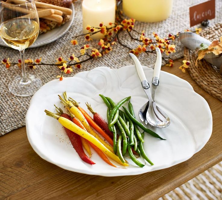 a white plate topped with green and red peppers next to a glass of wine on top of a wooden table