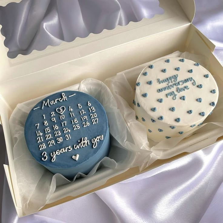 two cupcakes in a box with blue frosting and writing on the side