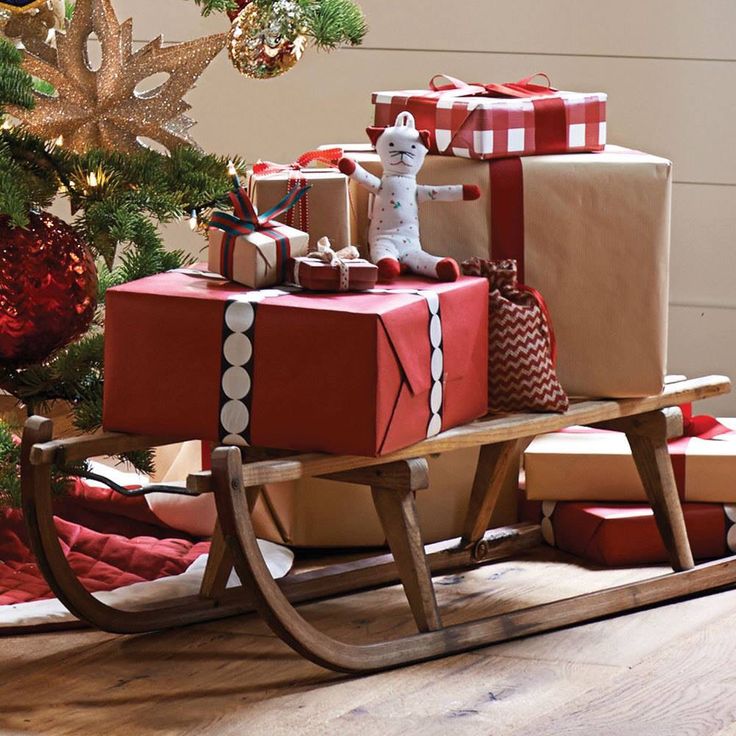 a wooden sleigh with presents on it in front of a christmas tree