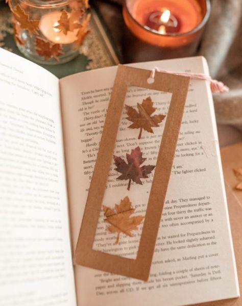 an open book sitting on top of a table next to a candle and some leaves