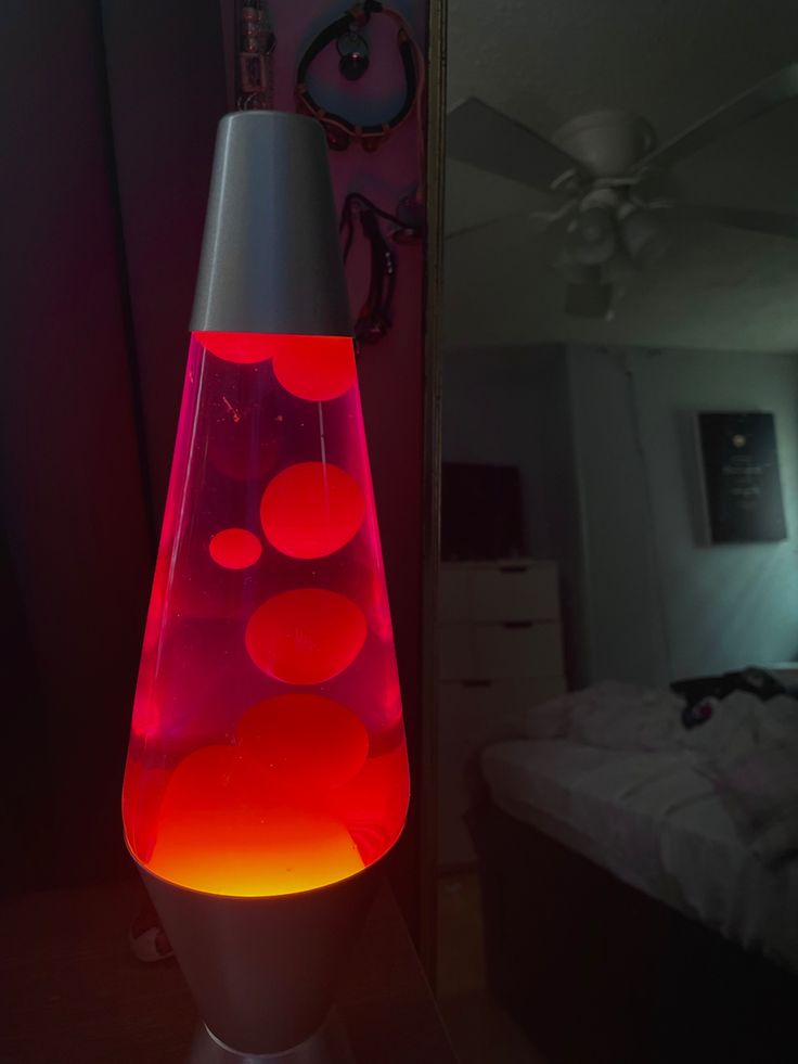 a red and orange lamp sitting on top of a wooden table next to a bed