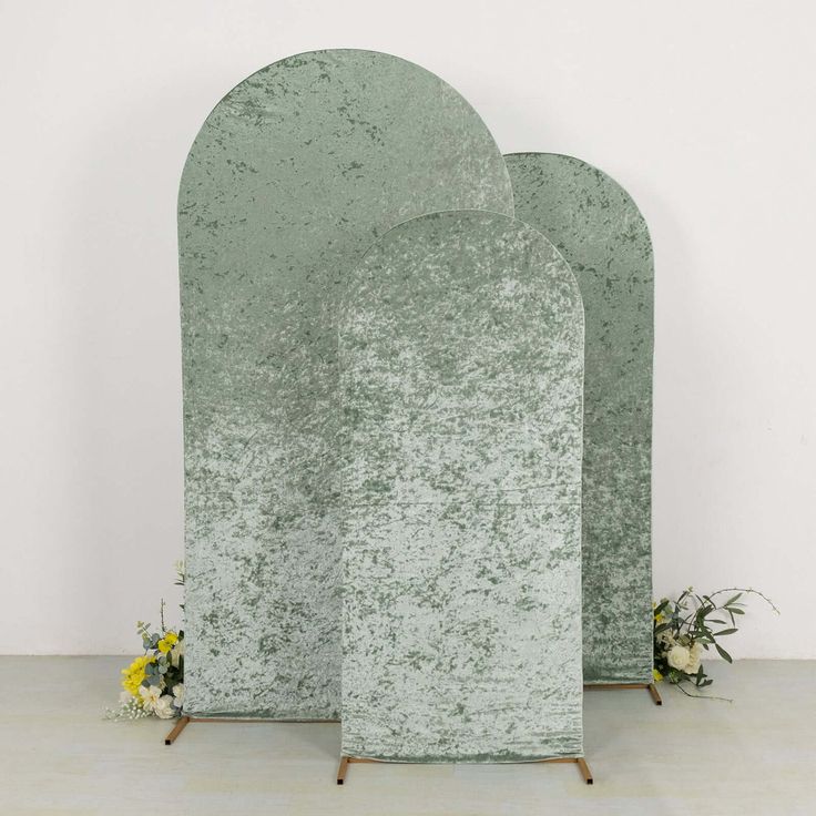 three green stone sculptures sitting on top of a white floor next to flowers and vases