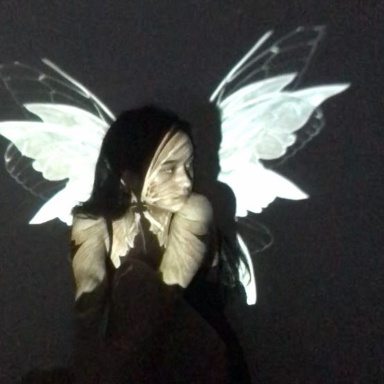 a woman with white wings on her body in the dark, looking up at something