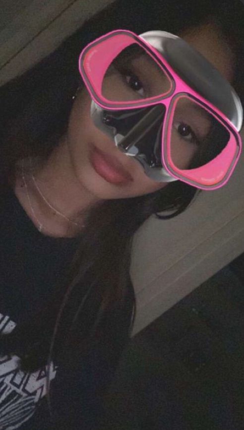 a woman wearing pink goggles and a black t - shirt is taking a selfie