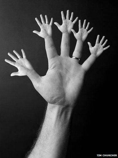 several hands reaching up into the air to reach something in black and white photo with dark background