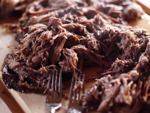 shredded meat sitting on top of a cutting board with a knife and fork in it