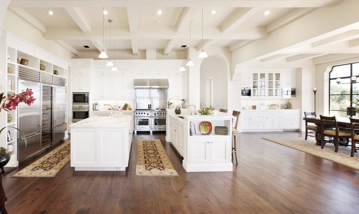 a large open kitchen and dining room with hardwood floors, white walls and ceiling beams