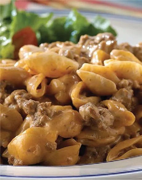 a white plate topped with pasta and meat covered in sauce next to a green leafy salad