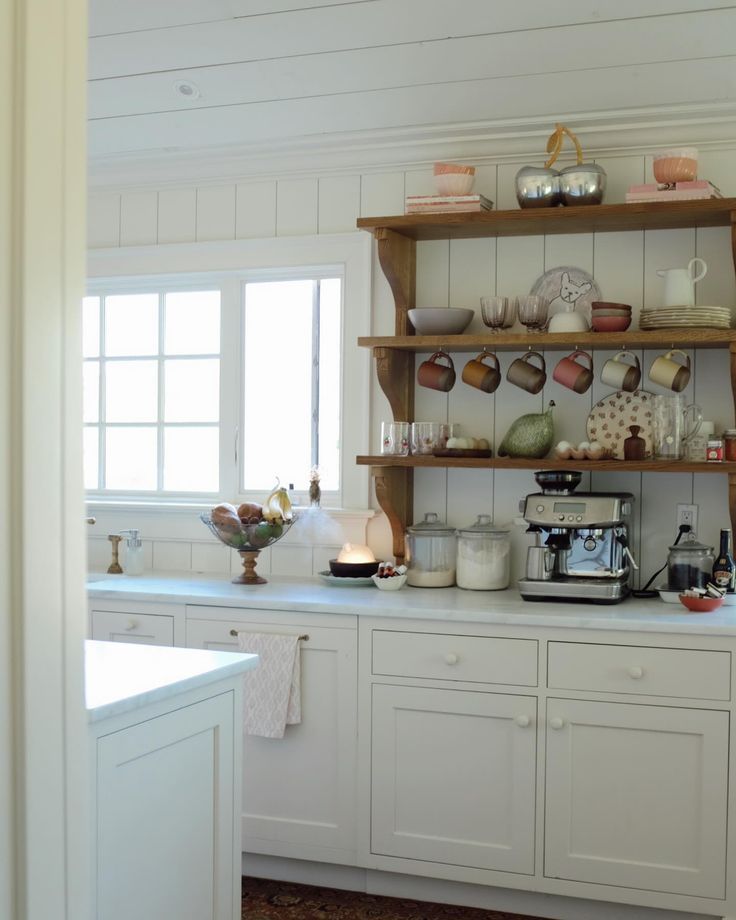 a kitchen with white cabinets and shelves filled with dishes