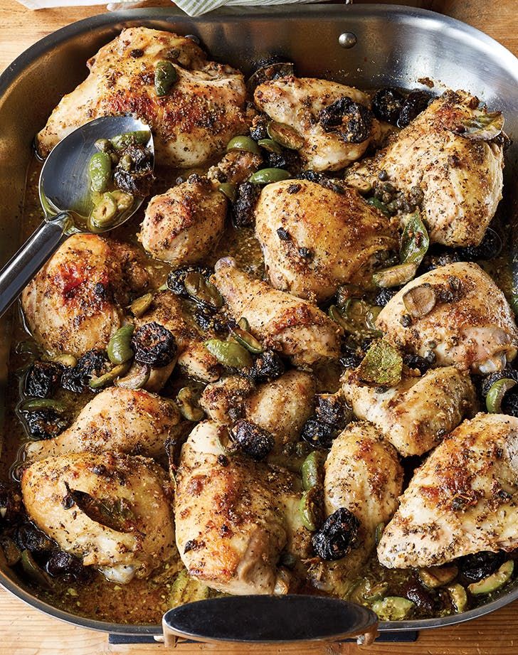 a pan filled with chicken and vegetables on top of a table next to a spoon