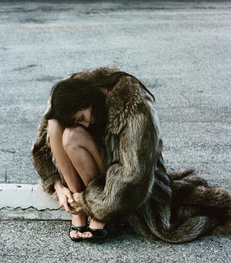 a woman sitting on the ground with her head in her hands, wearing a fur coat