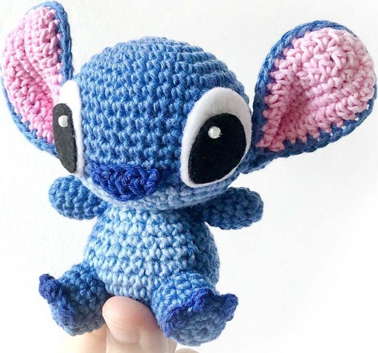 a small crocheted blue and pink stuffed animal with big eyes sitting in the palm of someone's hand