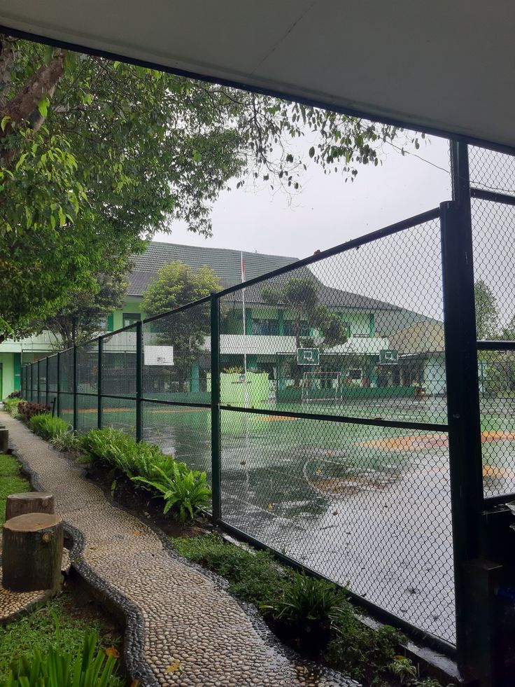 a tennis court is shown through a fenced in area with green grass and trees