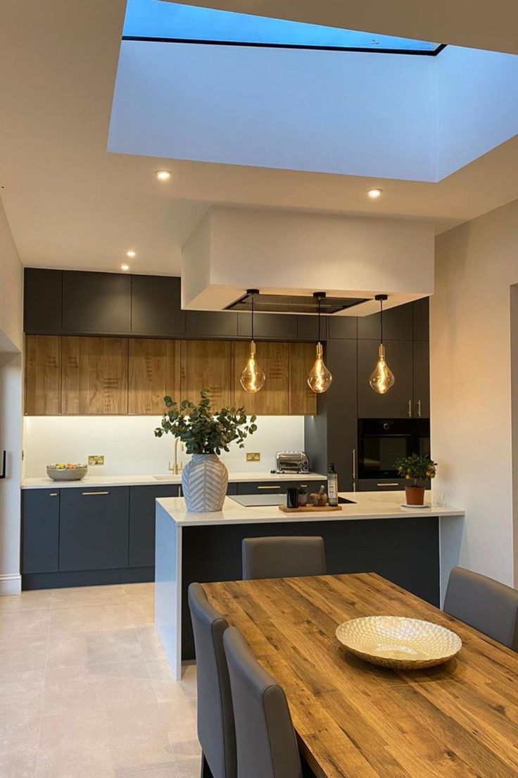 an open kitchen and dining room area with skylights above the countertop, along with a wooden table surrounded by gray chairs