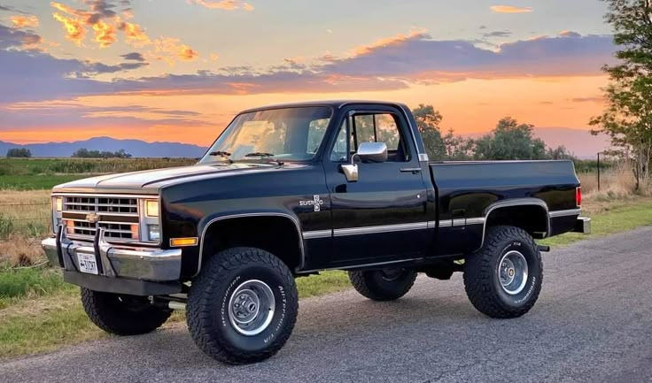 a black pickup truck parked on the side of a road in front of a sunset