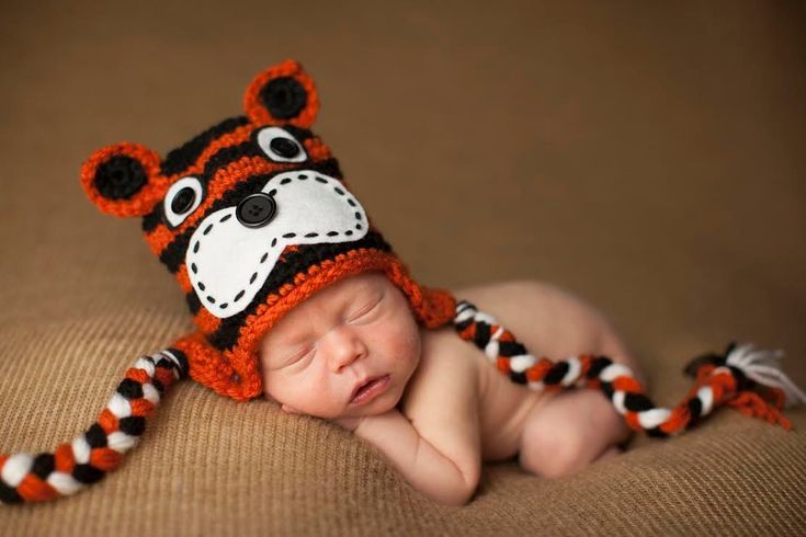 a baby wearing a tiger hat laying on top of a brown blanket