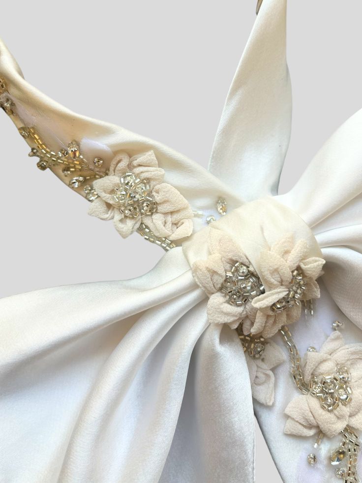 Available for pre-order, the expected ship date is Monday, December 18th. Our most elegant bow is now available in multiple sizes, with stunning hand embroidery for any big event. With hand-crafted flowers that add dimension against a supple silk backdrop, it's a truly standout accessory. Style with a strapless gown or top to highlight the stunning shape. Highlight the pink flower details with nice jewelery. Size 1: 12"-14" Size 2: 14"-16" Elegant Organza Bridal Accessories For Ceremony, Elegant Cream Bow For Parties, Elegant Cream Bow For Party, Luxury Satin Bow For Evening, Cream Satin Bow For Wedding, Luxury Satin Bow For Party, White Embroidered Bridal Accessories For Party, Silk Backdrop, Crafted Flowers