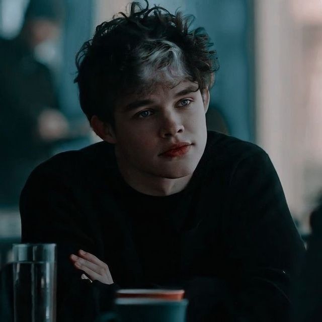 a young man sitting at a table in front of a cup