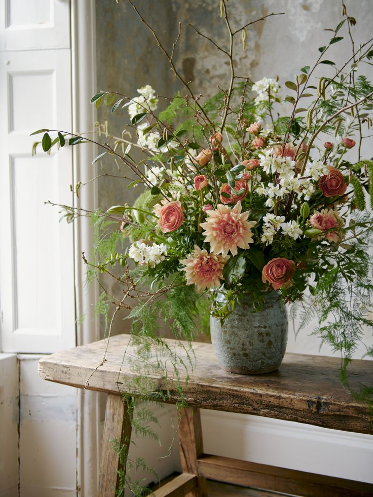 a vase filled with lots of flowers sitting on top of a wooden table next to a window