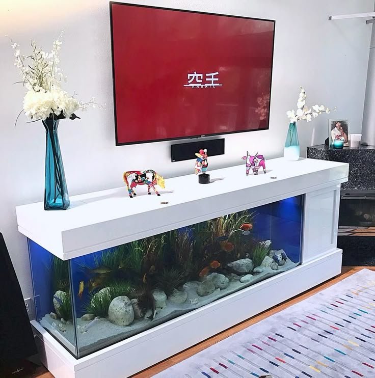 a fish tank sitting on top of a white table next to a tv mounted above it