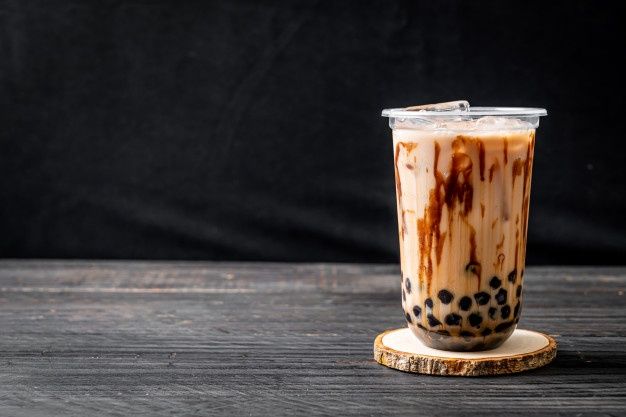 a drink in a plastic cup sitting on top of a wooden coaster next to a black background