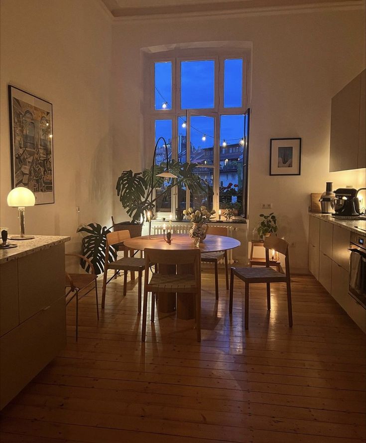 a dining room table and chairs in front of a window with the city lights outside