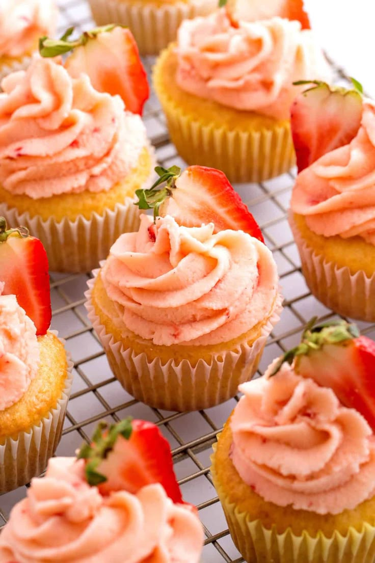 several cupcakes with pink frosting and strawberries on top are sitting on a cooling rack